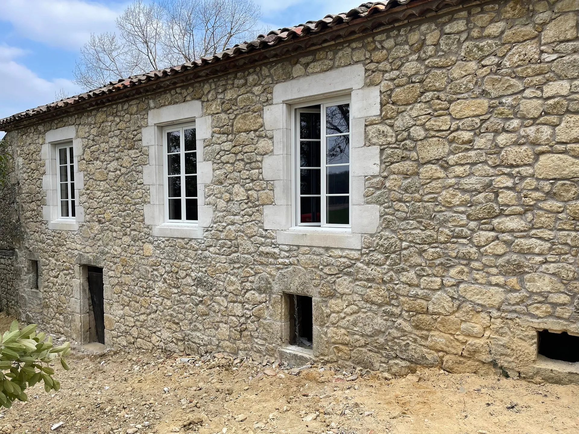 Façade en pierre rénovée : moellons rejointoyés, encadrements de fenêtres en pierre de taille, fenêtres neuves