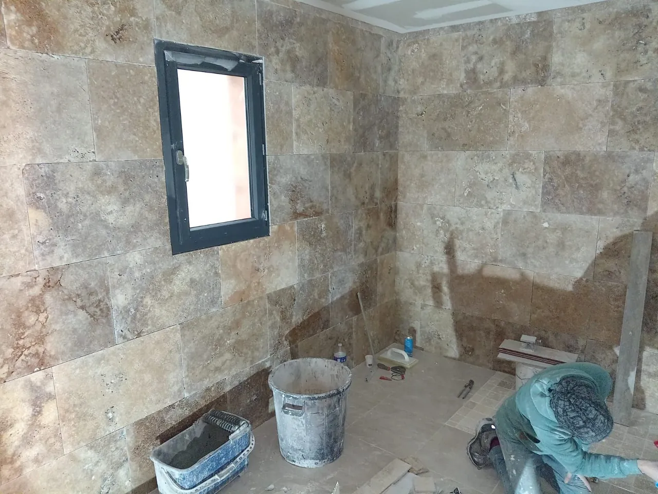 Pièce aux murs habillés de carreaux de pierre aspect travertin, en cours de pose