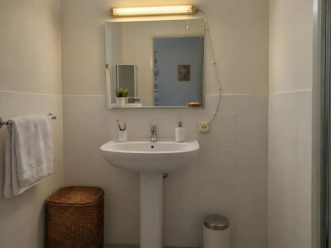 Lavabo sur colonne sous un miroir, vieille réglette jaunie, fil blanc apparent qui descend jusqu'à une prise en saillie