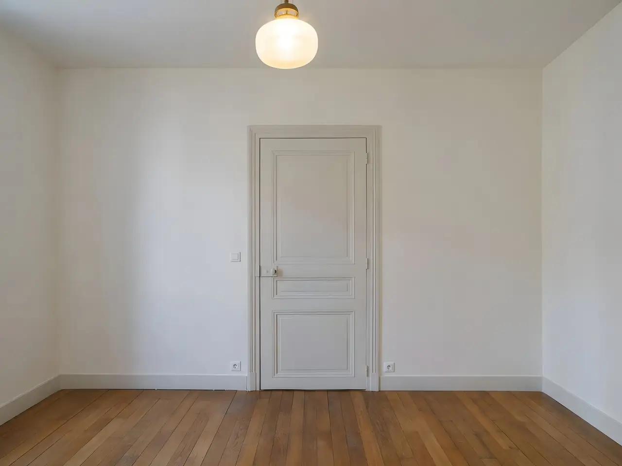 Chambre aux murs blancs sans fil apparent, plafonnier en verre allumé, interrupteur et prises encastrés près de la porte
