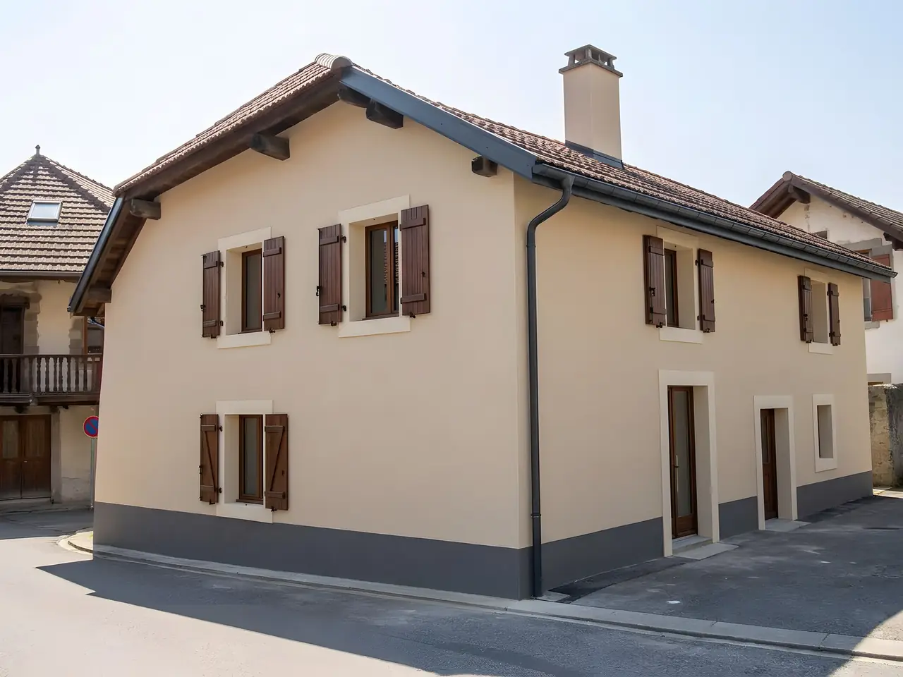 La même maison de village enduite de neuf en beige, volets bruns et soubassement gris