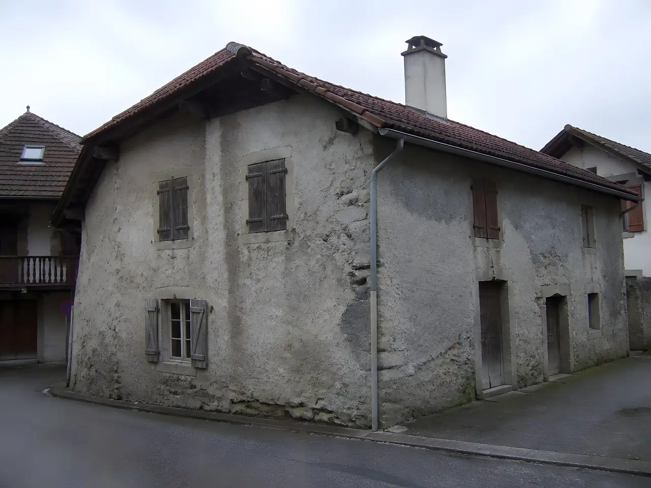 Maison de village ancienne à l'enduit gris encrassé, décollé par plaques, volets en bois délavés
