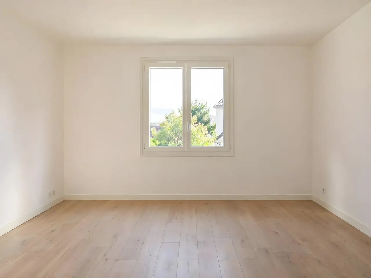 Chambre vide aux murs et au plafond blanc chaud, fenêtre à deux vantaux au fond, parquet clair, plinthes blanches