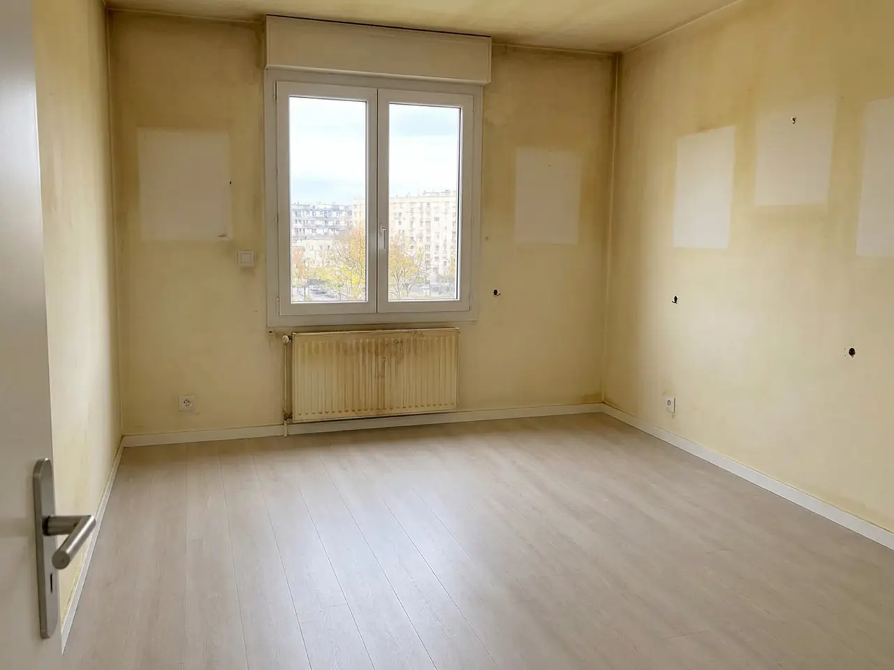 Pièce vide aux murs jaunis, rectangles clairs laissés par les cadres et trous de chevilles, avant remise en état