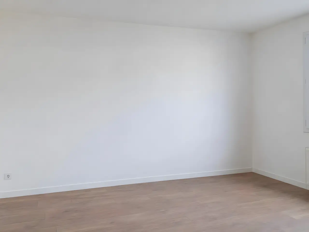 Mur de chambre lisse et blanc, d'un seul ton jusqu'à l'angle, au-dessus d'une plinthe blanche et d'un parquet