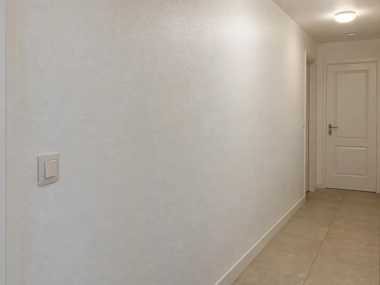 Mur de couloir couvert d'une toile de verre peinte en blanc satiné, trame fine et régulière, porte blanche au fond