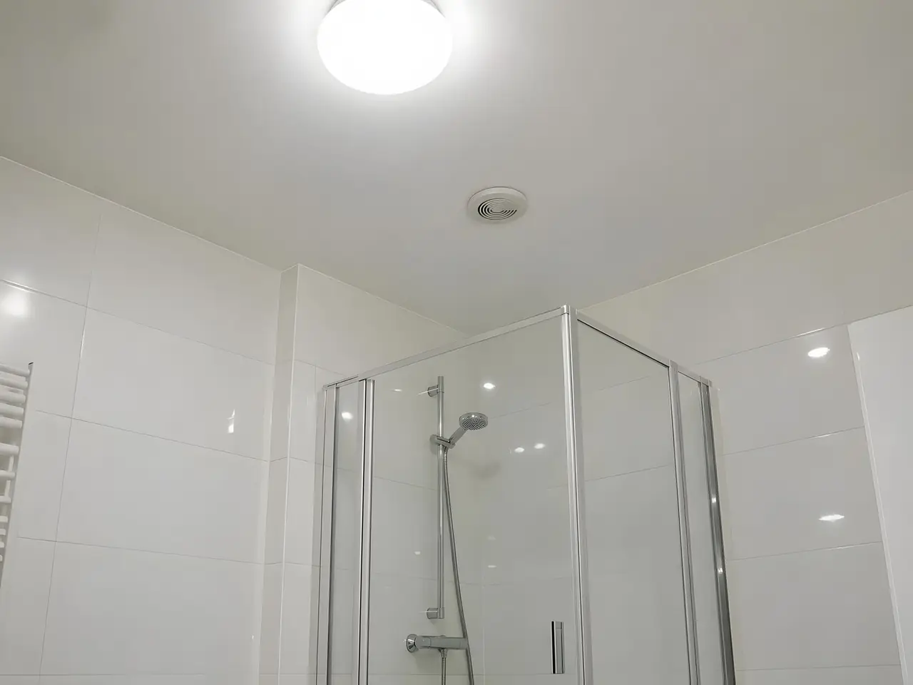 Plafond de salle de bains blanc net au-dessus d'une douche vitrée, bouche d'aération propre, faïence blanche
