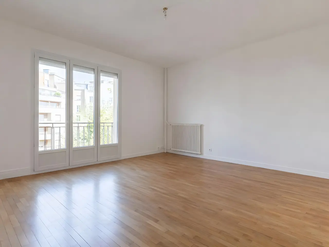 Séjour vide aux murs et au plafond d'un blanc net, grande porte-fenêtre lumineuse et parquet clair