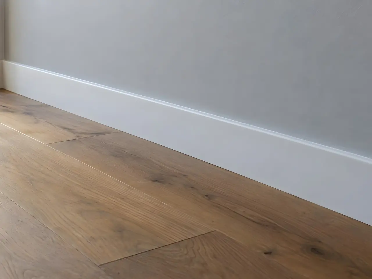 Plinthe laquée blanc satiné, nette et régulière, au pied d'un mur gris clair sur un parquet en chêne intact
