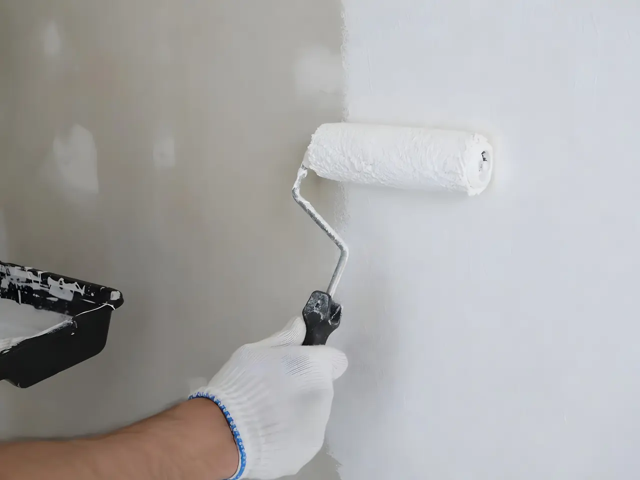 Main gantée qui passe un rouleau de peinture blanche sur un mur, la partie couverte nette à côté de l'enduit brut