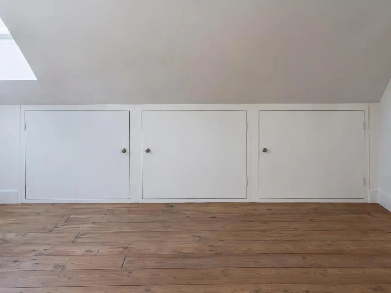 Chambre sous les combles, rampant blanc posé sur un petit mur bas percé de trois portes de placard blanches