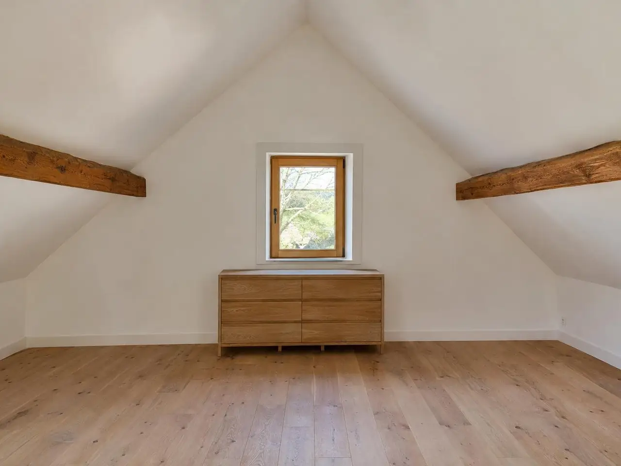 Comble aménagé au pignon blanc et lisse, petite fenêtre en bois habillée, pentes blanches, commode en chêne