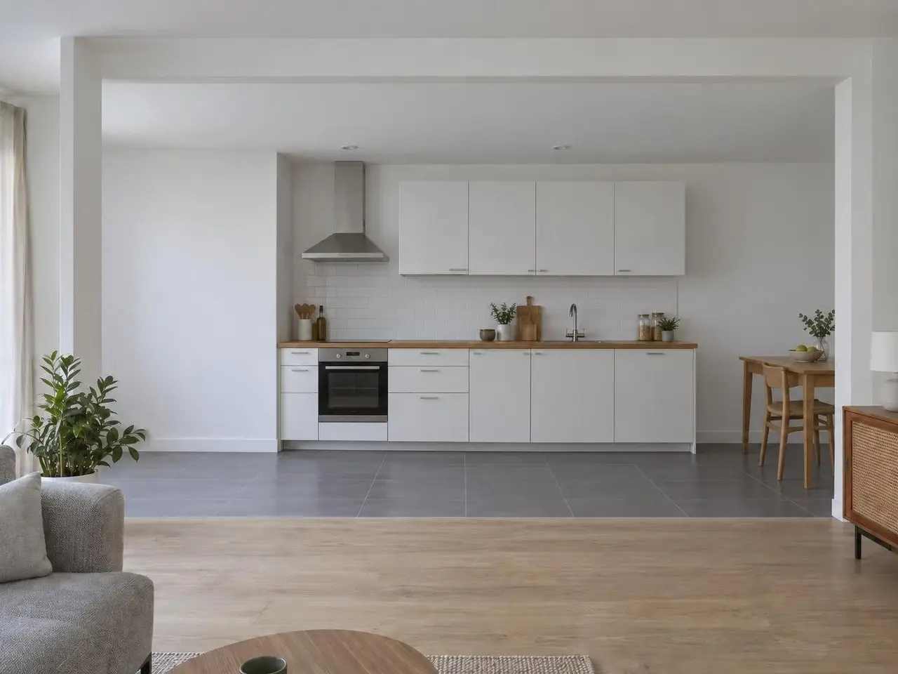 Séjour au parquet clair ouvert sur une cuisine blanche en ligne avec four, hotte inox et petite table