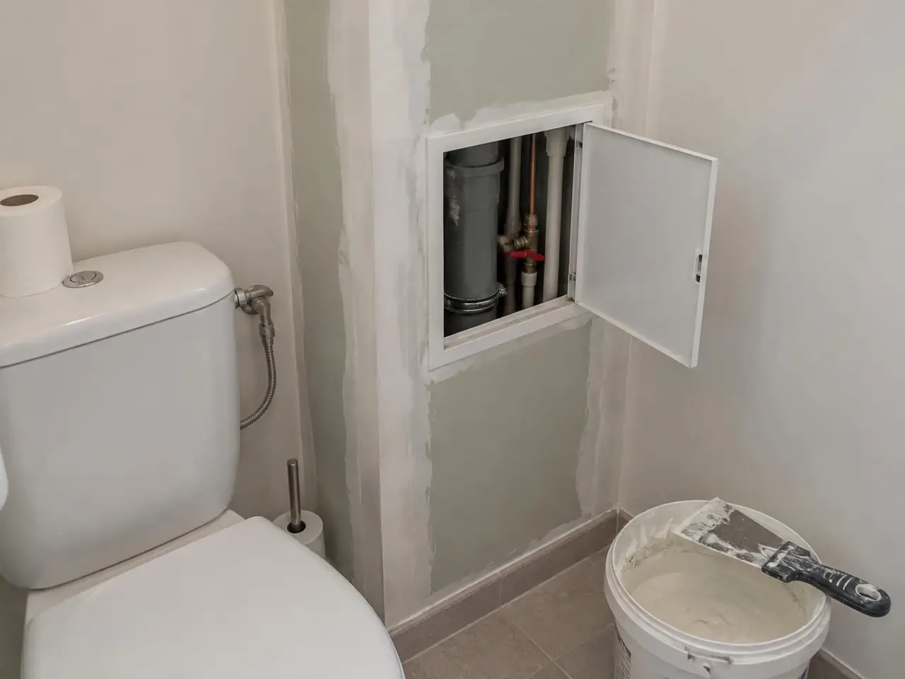 Coffrage en plaques dans des toilettes, trappe de visite ouverte sur la descente d'eau, les tuyaux et une vanne