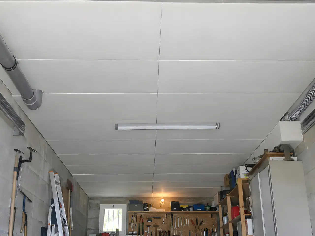 Le même garage avec un plafond fini en panneaux isolants blancs jointifs, néon et gaines remis en place