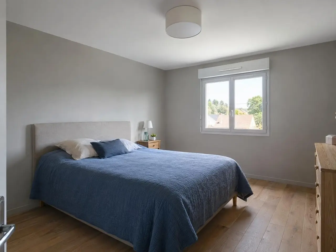 Chambre sous le grenier au plafond neuf d'un blanc uniforme, plafonnier rond, lit à couverture bleue