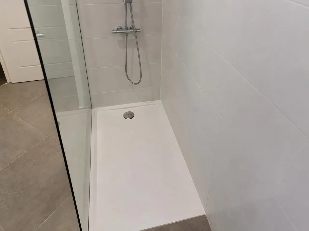 Receveur de douche blanc propre et sec, bonde chromée bien nette, paroi vitrée et faïence blanche autour