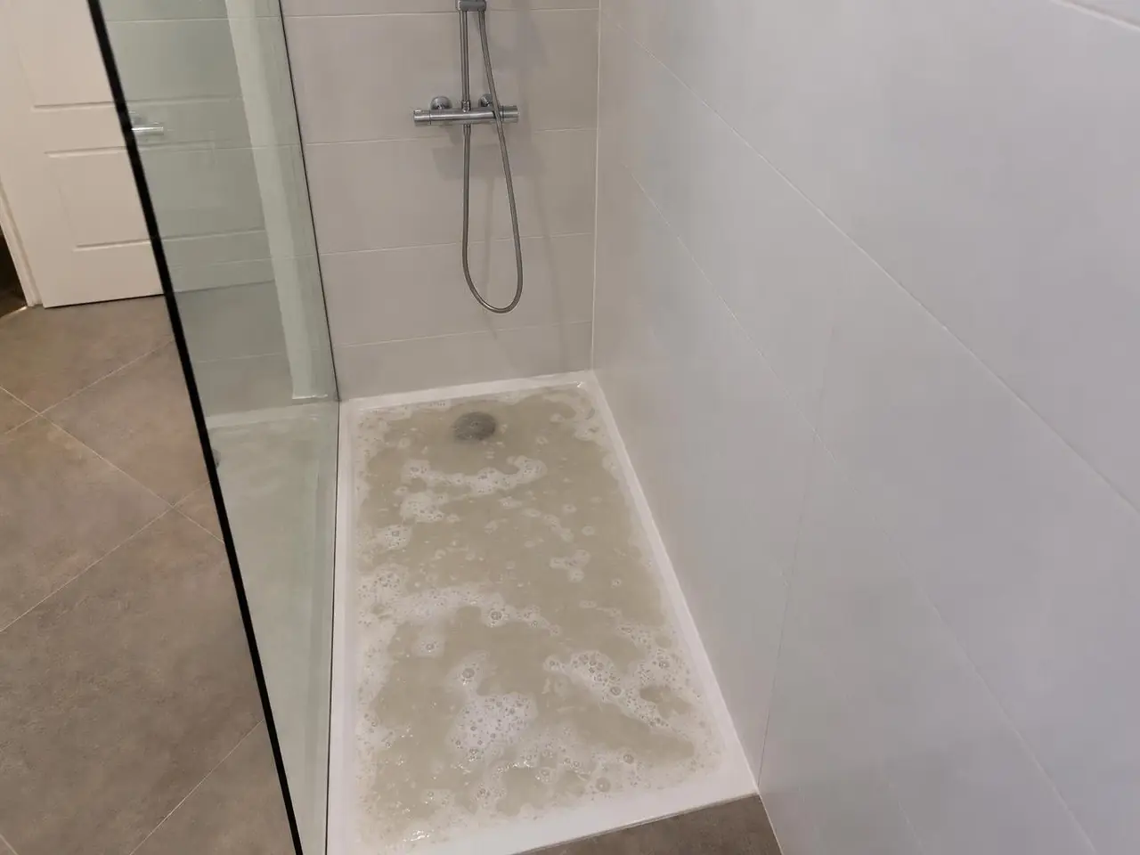 Receveur de douche blanc rempli d'eau grisâtre et savonneuse qui stagne, bonde à peine visible au fond