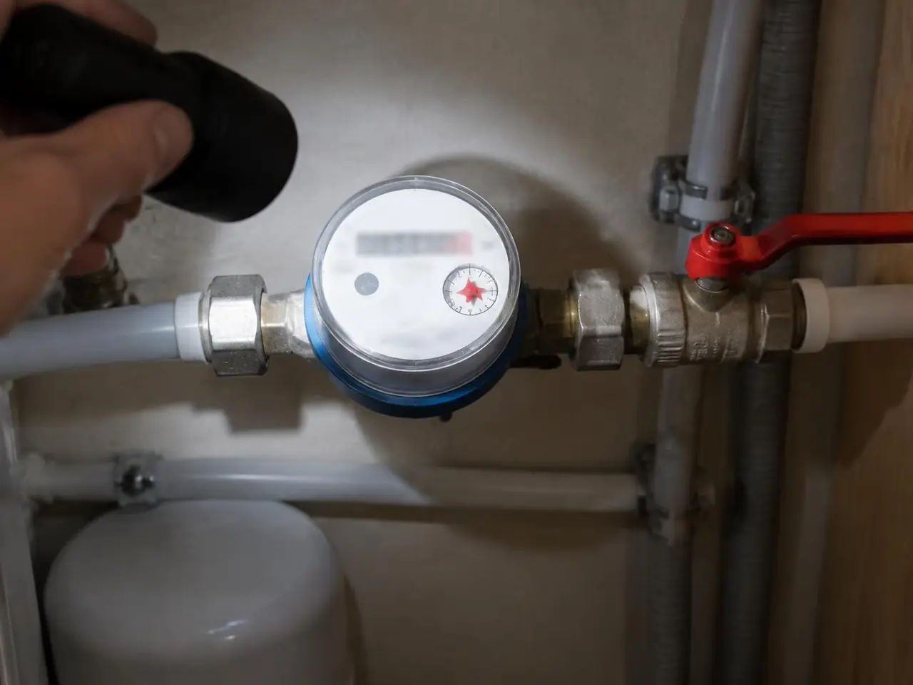 Lampe braquée sur un compteur d'eau, l'étoile rouge du cadran visible, robinet d'arrêt à manette rouge à côté