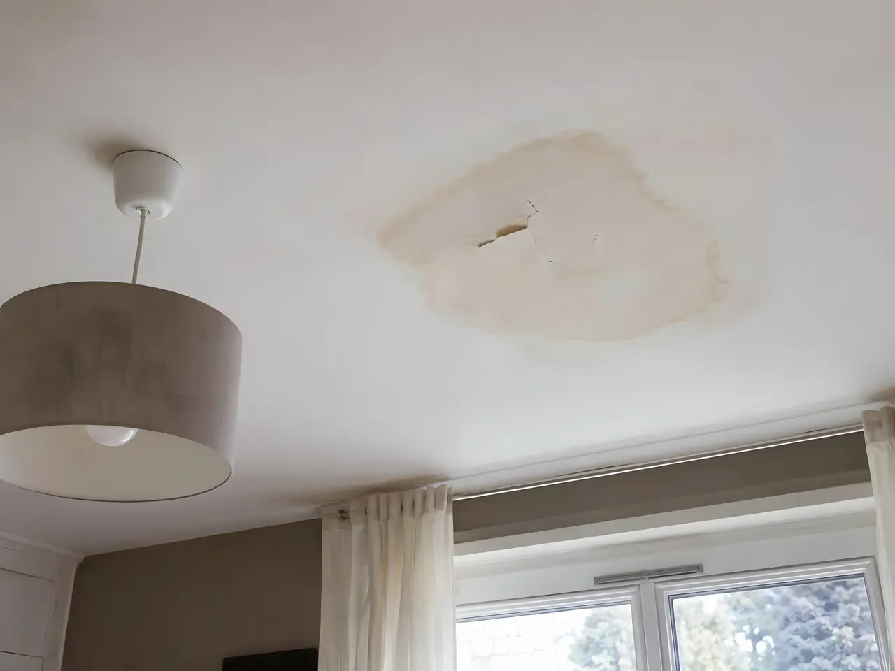 Plafond blanc marqué d'une grande auréole jaunâtre de dégât des eaux, près d'une suspension en tissu gris
