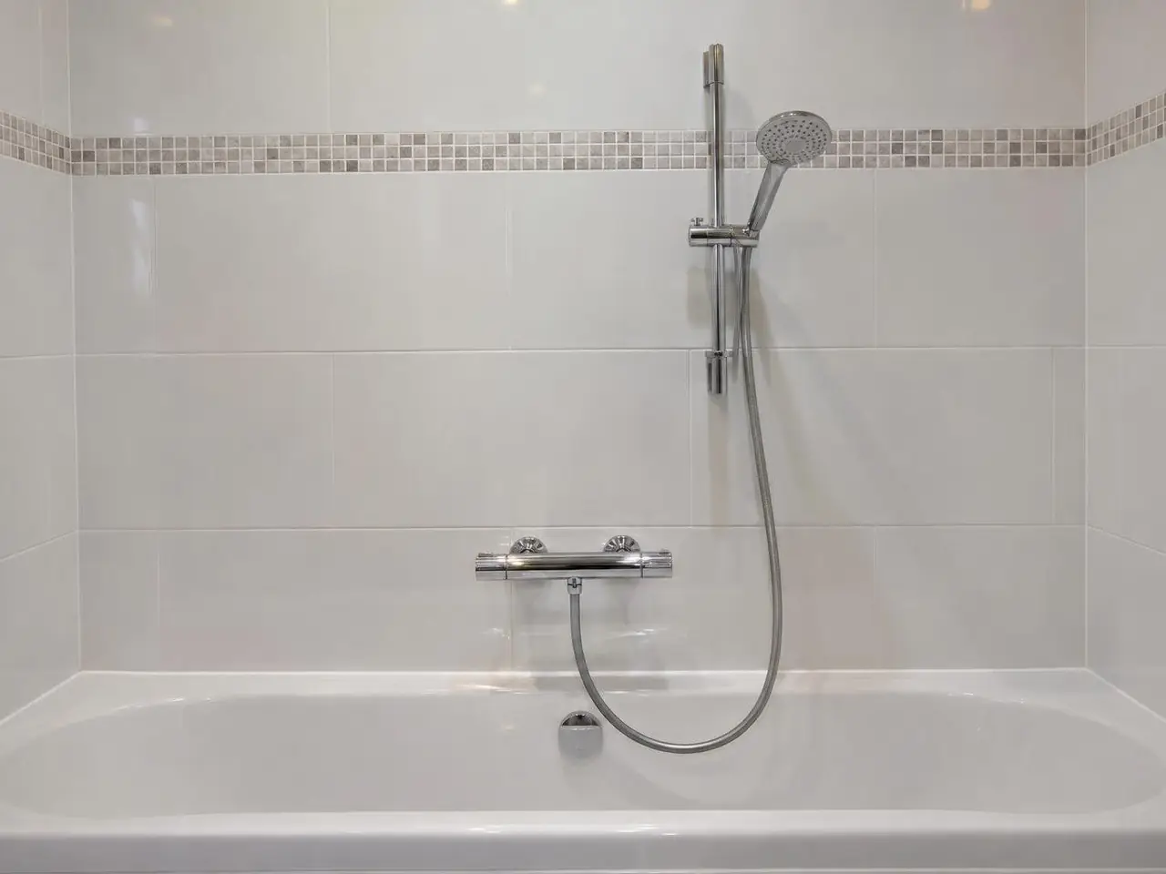 Mitigeur thermostatique chromé neuf au-dessus d'une baignoire blanche, flexible et douchette sur leur barre
