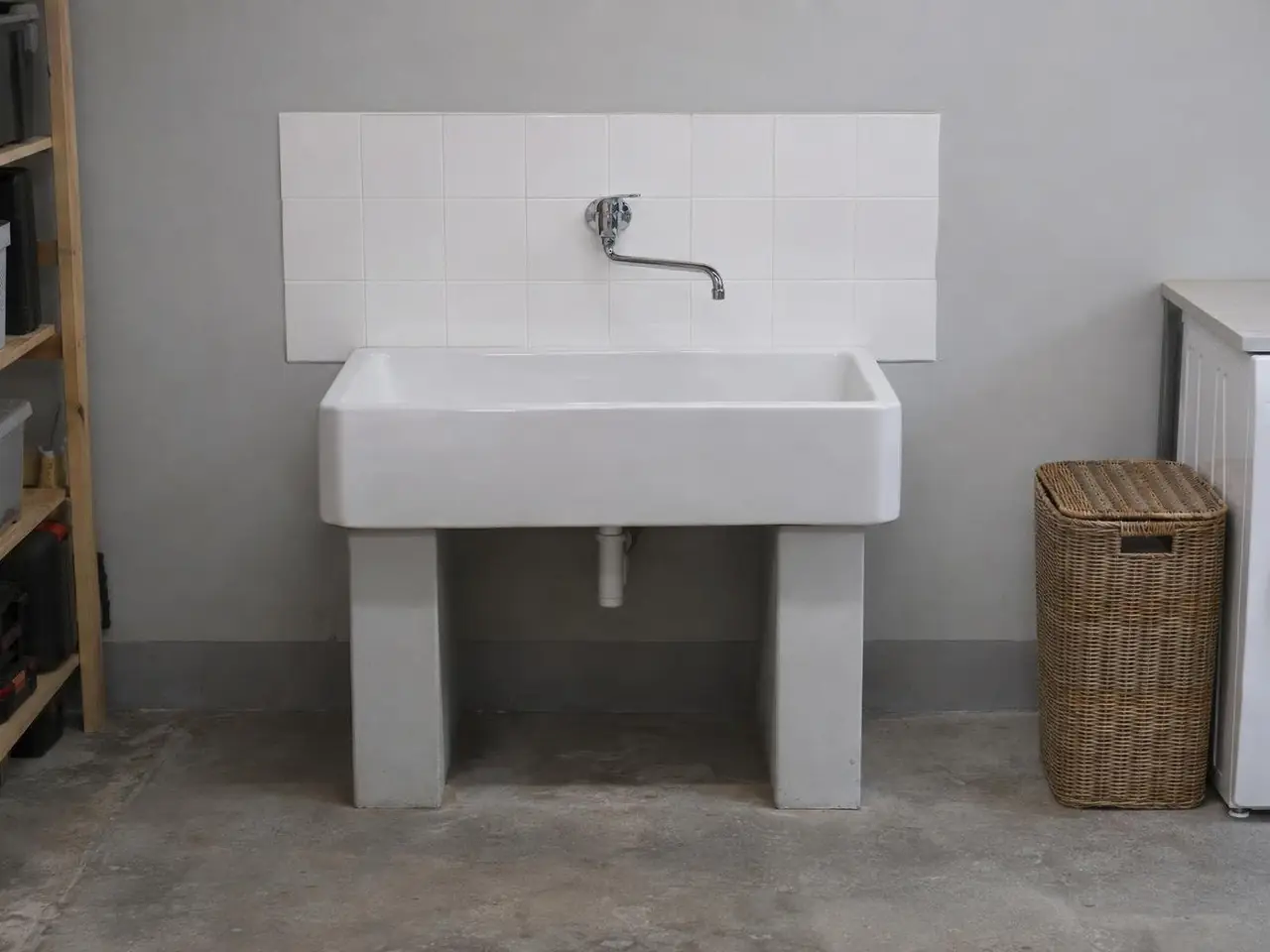 Bac à laver en grès blanc propre sous un robinet mural chromé neuf à bec long, carrelage blanc au-dessus