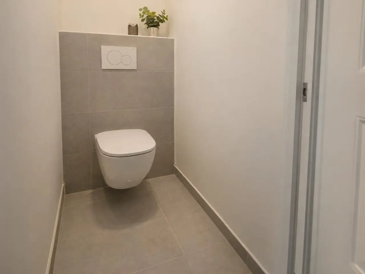 Petites toilettes, WC suspendu blanc devant un coffrage carrelé gris clair, plaque de commande à deux boutons